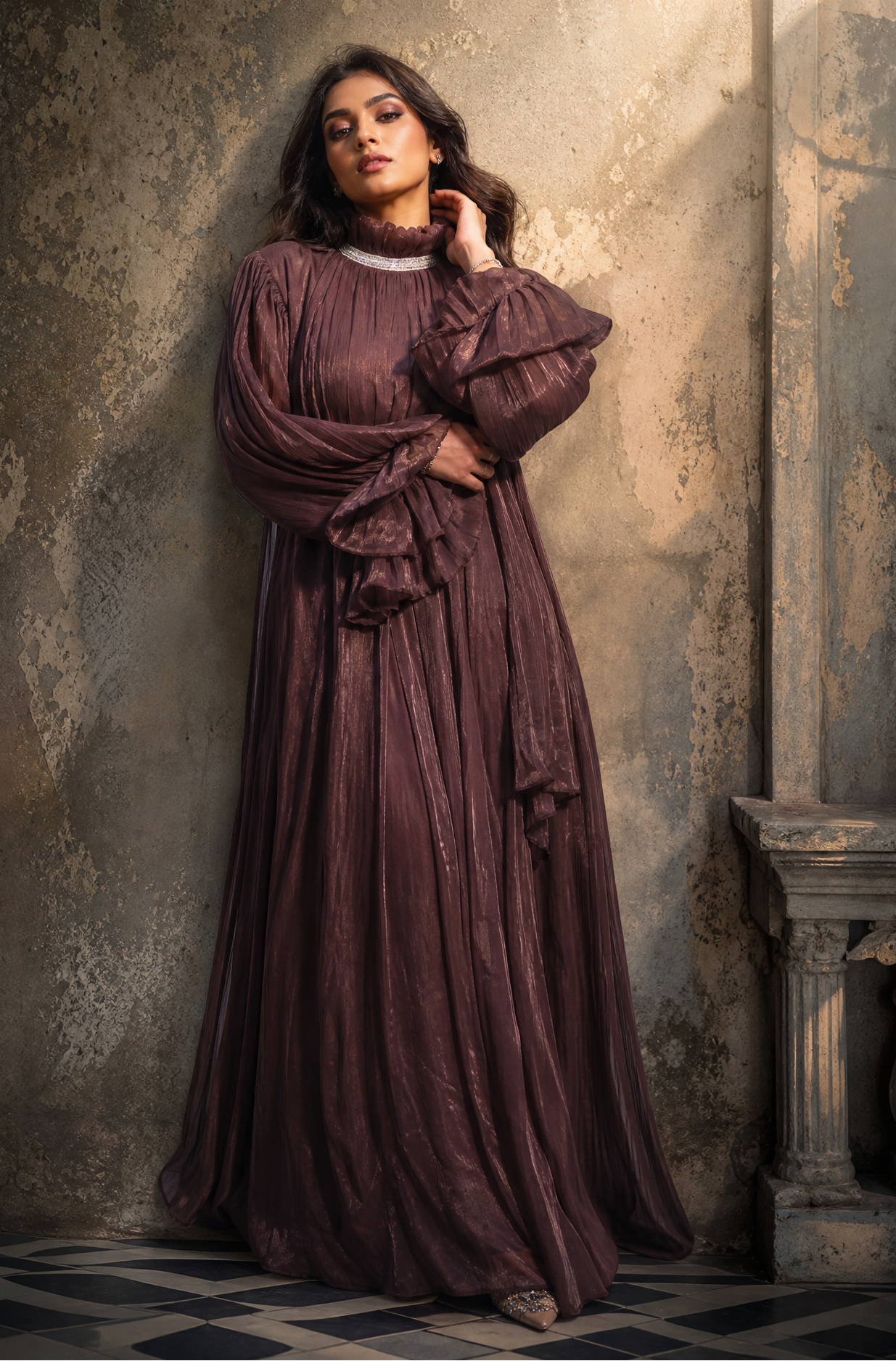 Woman in a long, dark purple dress standing against a textured wall.